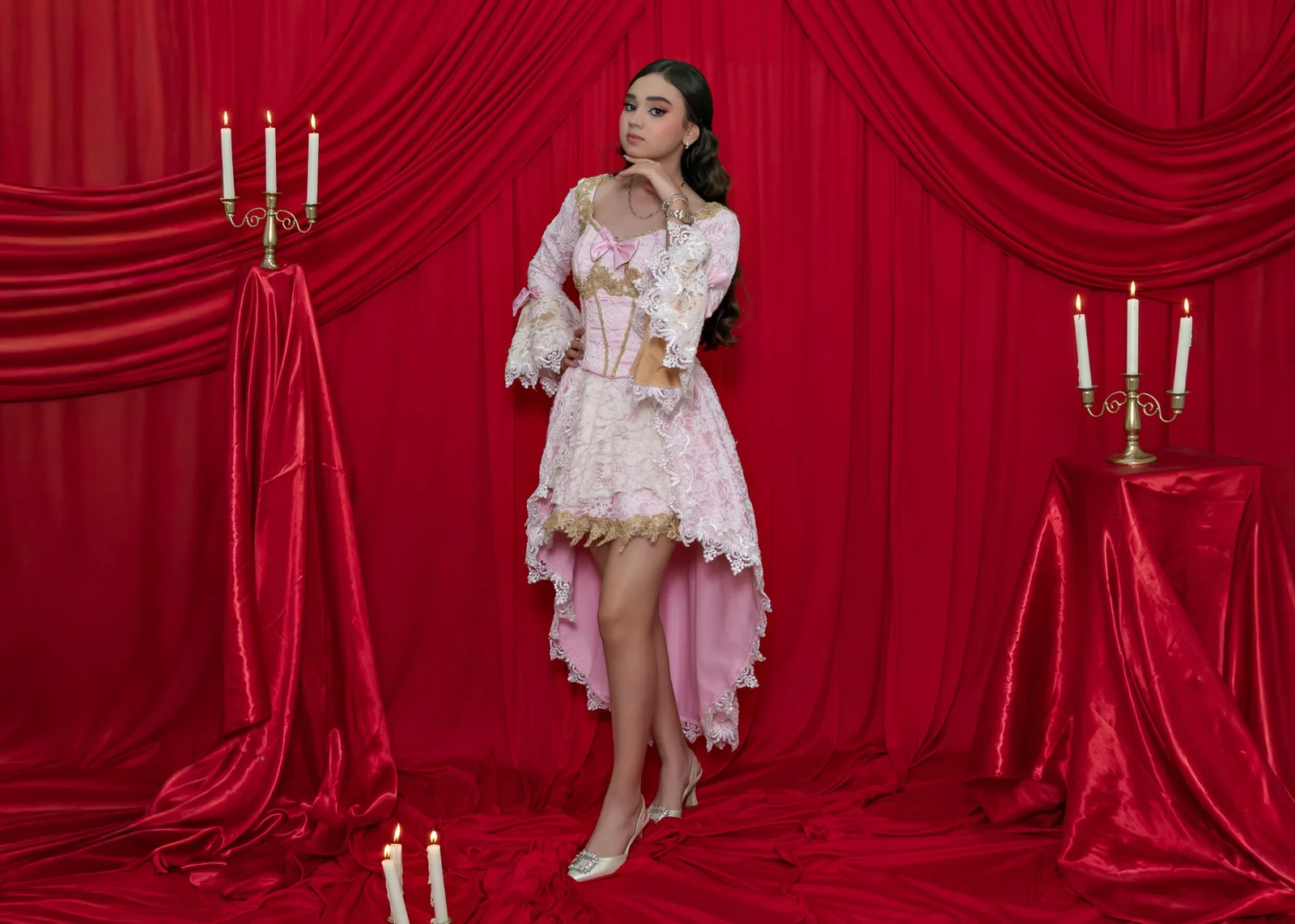 Joven con vestido rosa frente a cortinas rojas y candelabros.