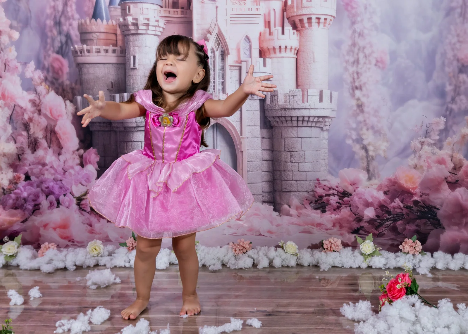 Niña con vestido de princesa rosa frente a un castillo.