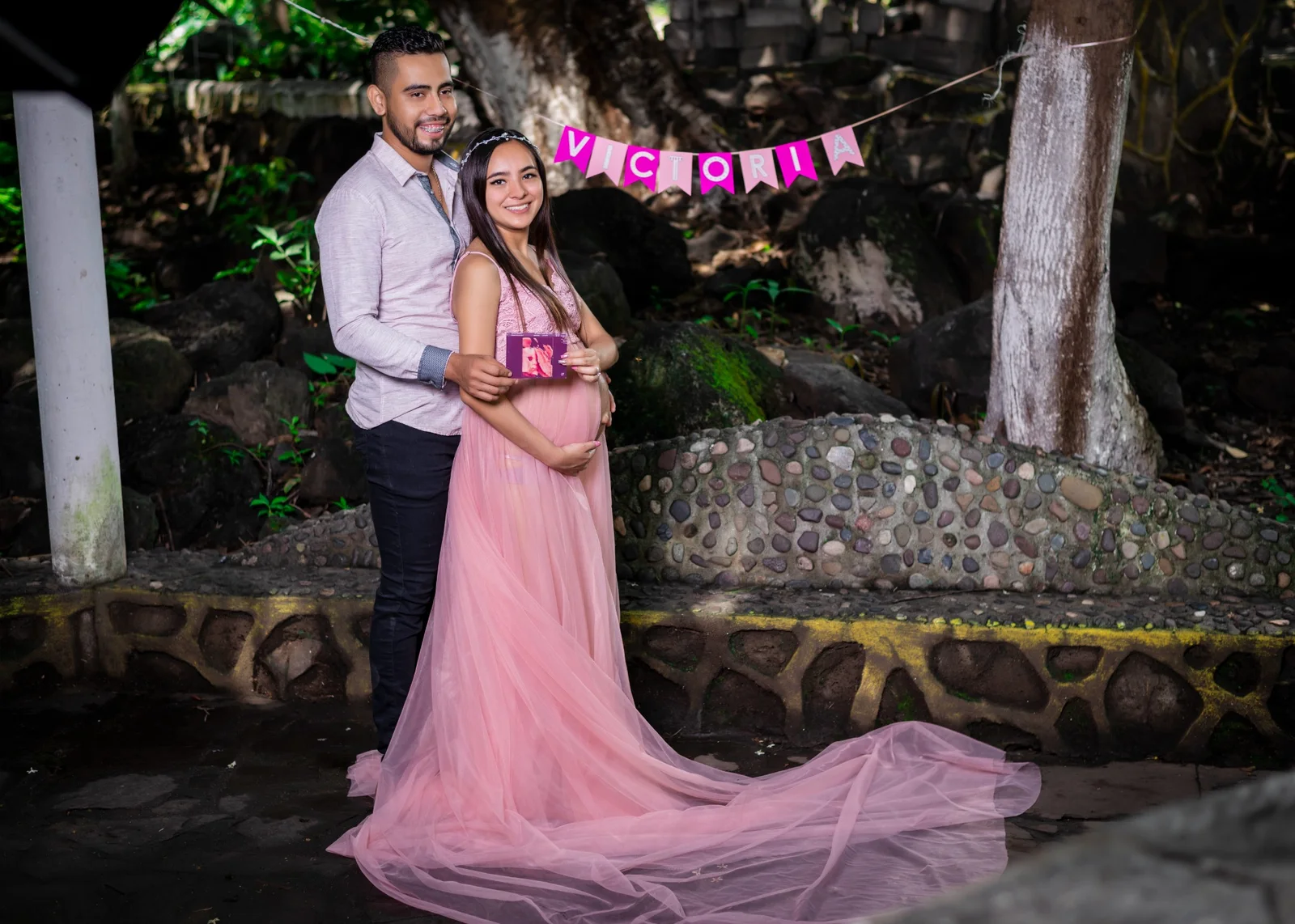 Pareja en sesión de maternidad en exterior con vestido rosa.