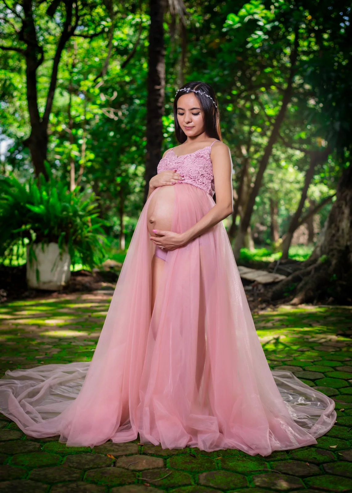 Retrato de maternidad en exterior con vestido rosa entre vegetación.