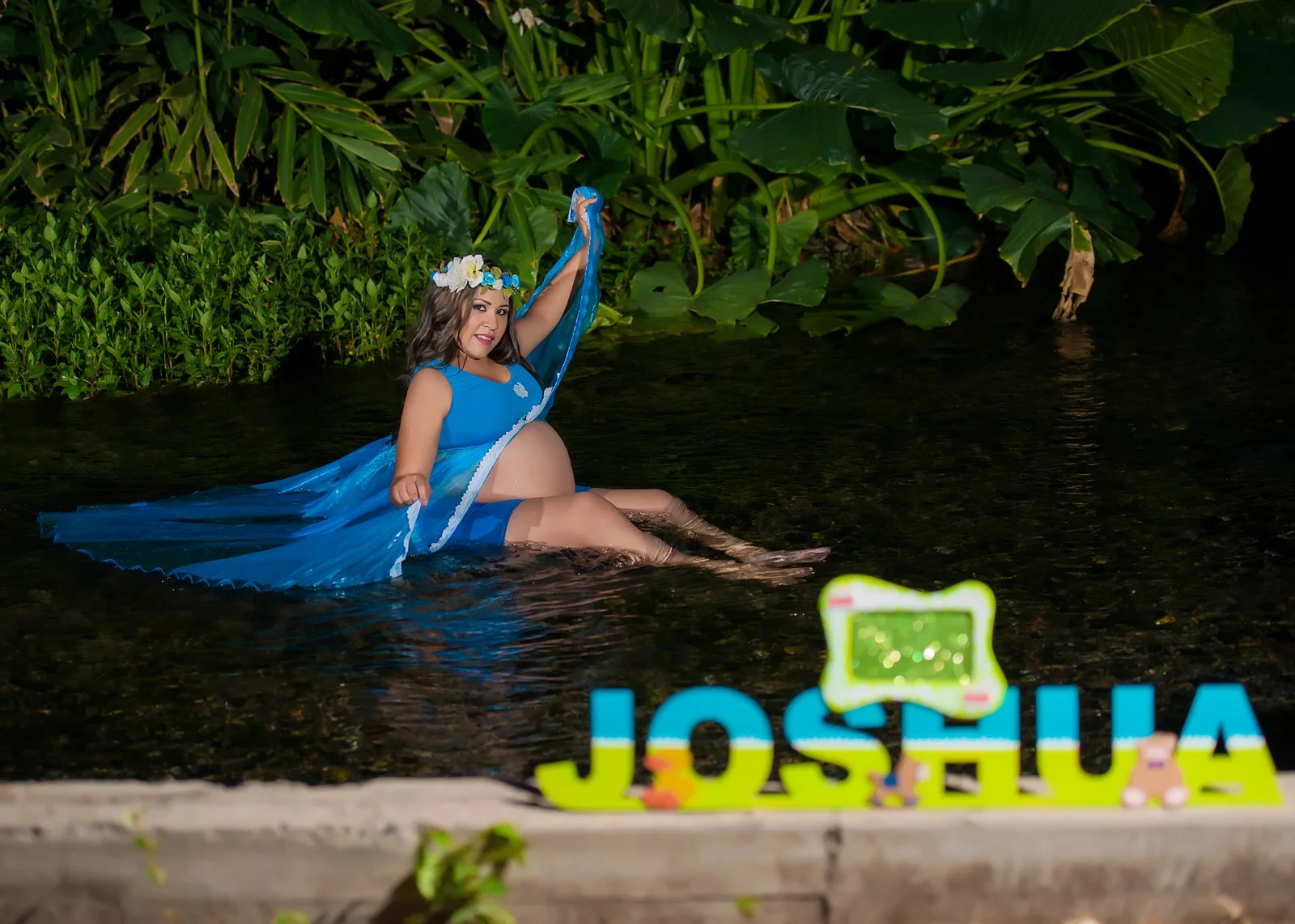 Retrato de maternidad en agua con vestido azul y nombre decorativo.