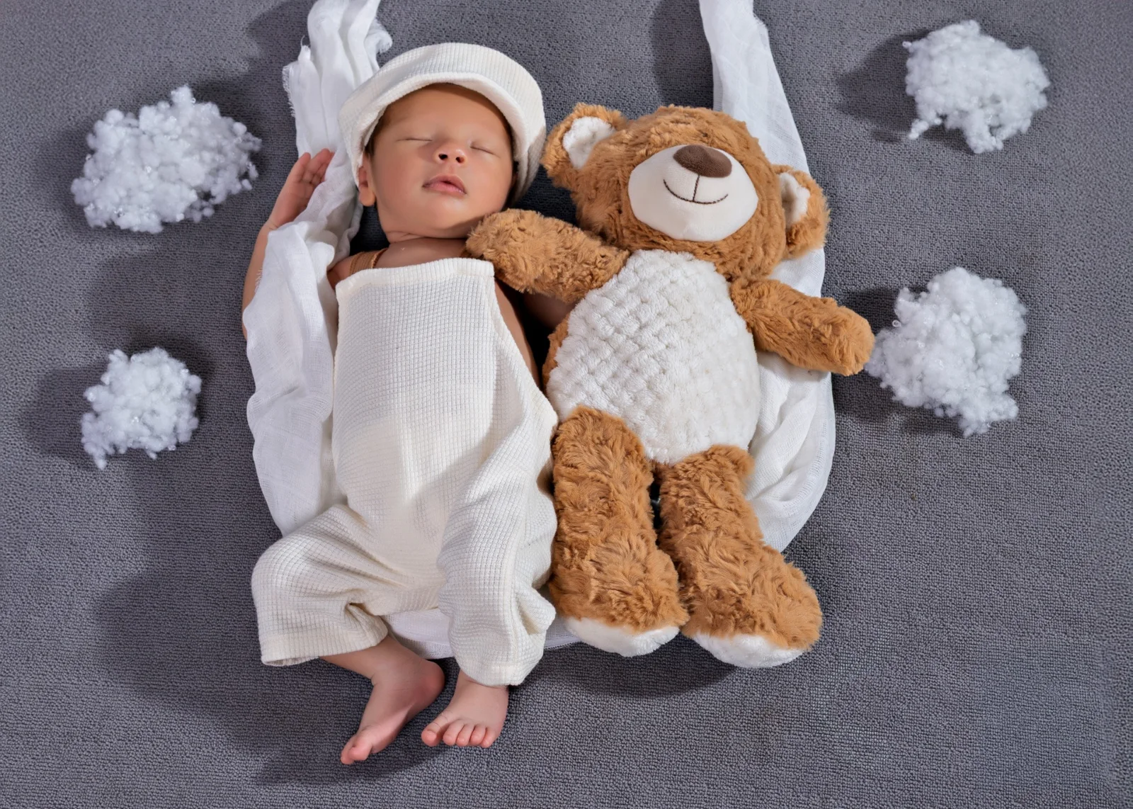 Bebé dormido junto a un oso de peluche sobre fondo gris en una sesión newborn.