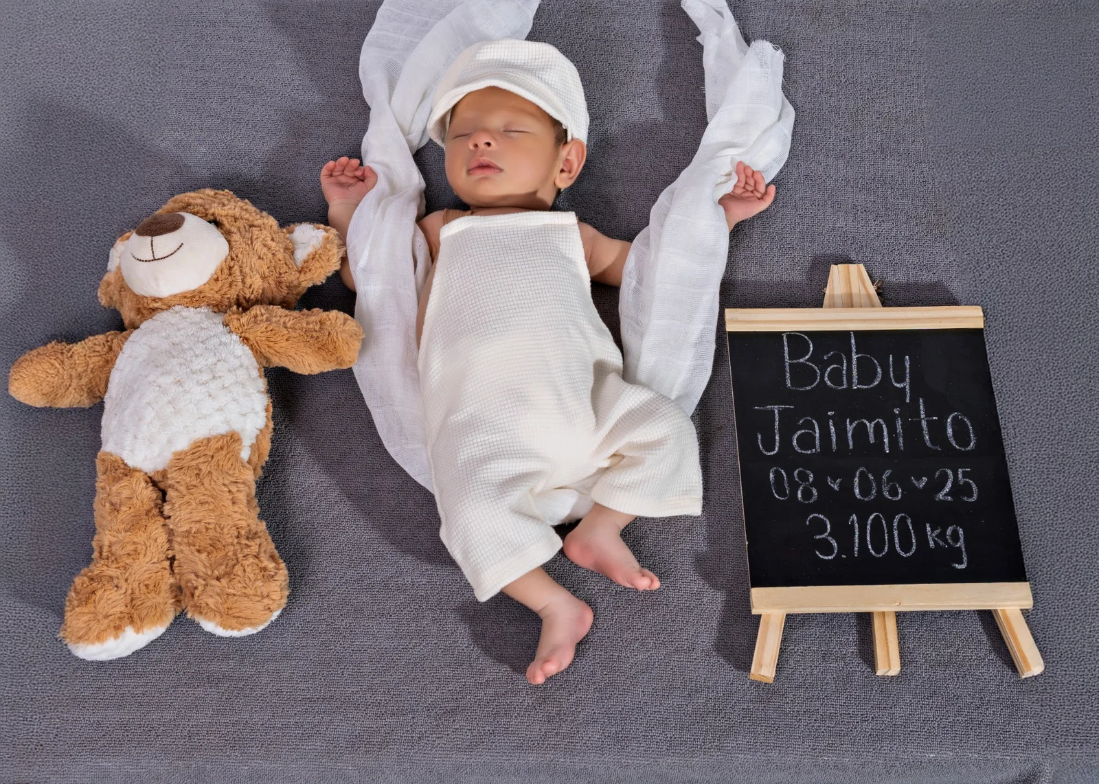 Bebé dormido junto a un oso de peluche y una pequeña pizarra en una sesión newborn.