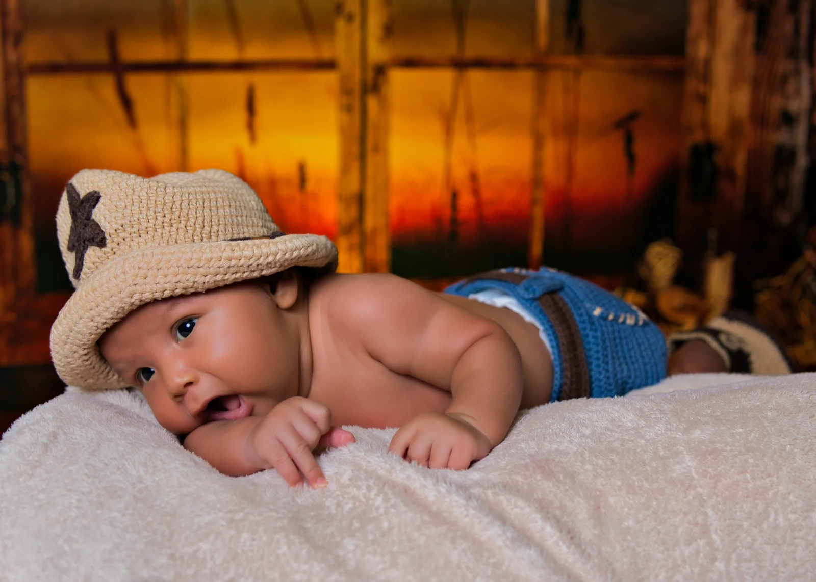 Bebé recostado con sombrero tejido en una sesión newborn de estilo western.