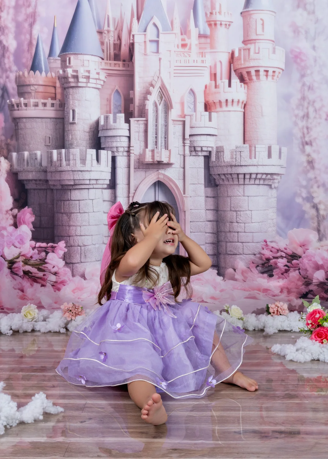 Niña con vestido lila jugando a cubrirse los ojos frente a un castillo.