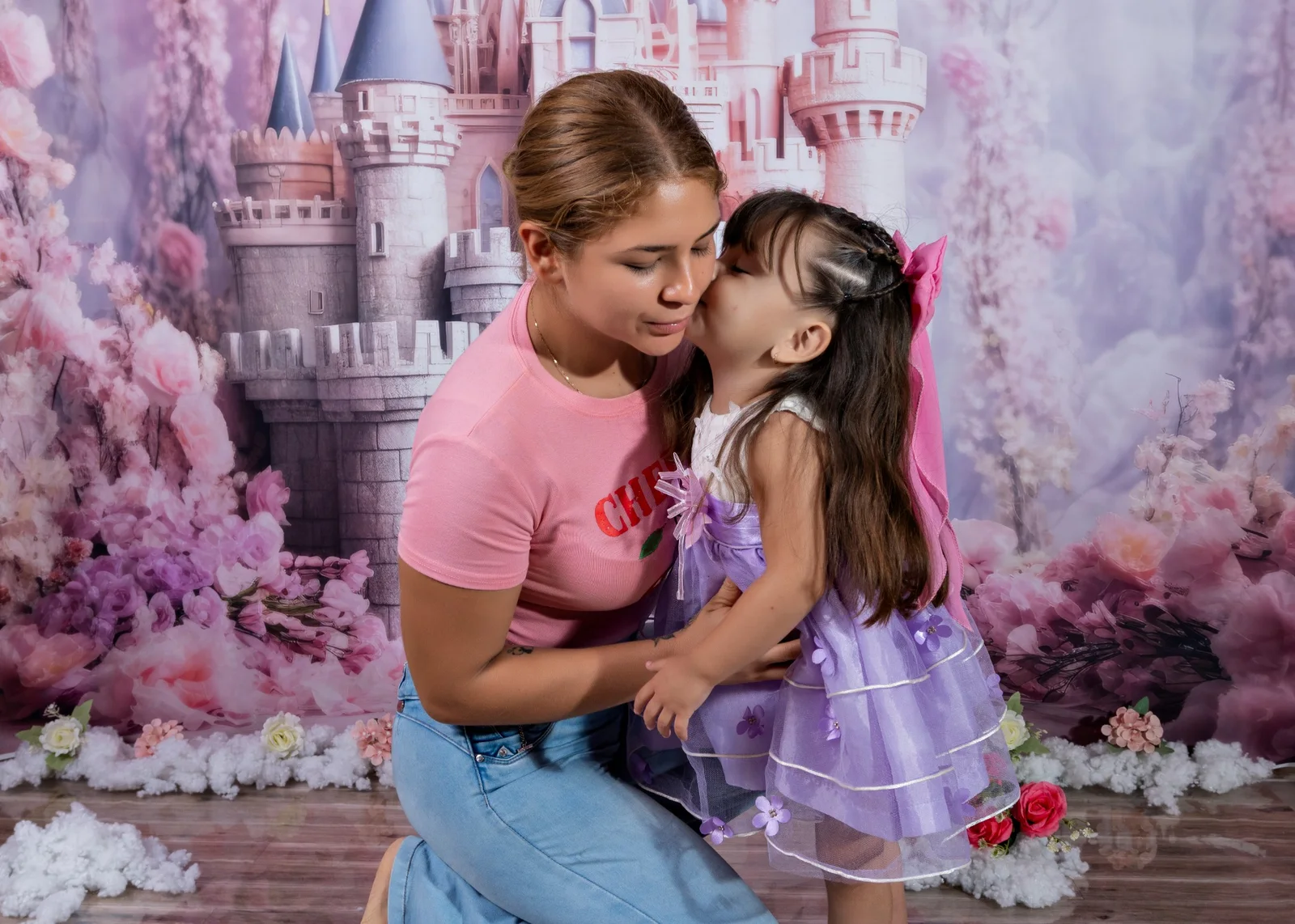 Niña con vestido lila dando un beso en la mejilla a una mujer durante la sesión infantil.